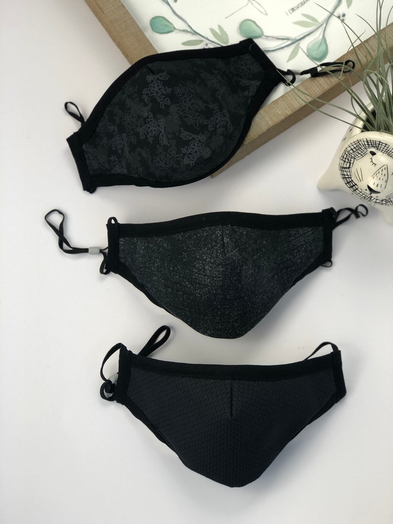 May include: Three black face masks with different patterns. The top mask has a floral pattern, the middle mask has a textured pattern, and the bottom mask has a mesh pattern.