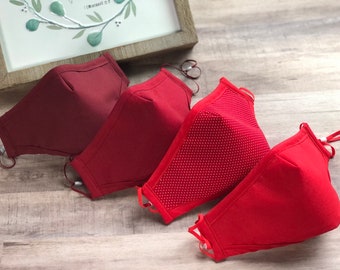 Op de afbeelding: Vier rode gezichtsmaskers, twee effen rood, een met witte stippen en een donkerder bordeauxrood.