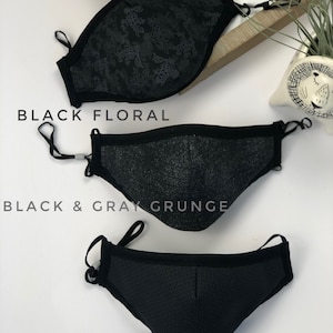 May include: Three black face masks with different patterns. The top mask has a black floral pattern, the middle mask has a black and gray grunge pattern, and the bottom mask has a black tiny flower pattern.