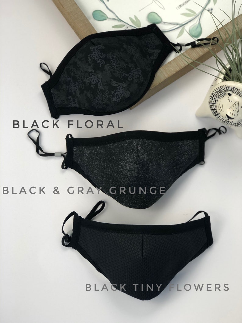 May include: Three black face masks with different patterns. The top mask has a black floral pattern, the middle mask has a black and gray grunge pattern, and the bottom mask has a black tiny flower pattern.