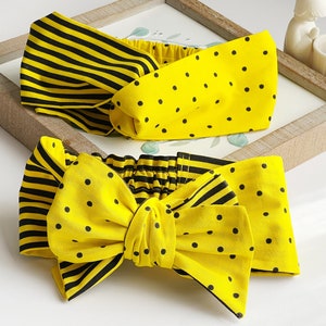 May include: Two yellow and black patterned headbands. One headband is striped and the other has black polka dots. Both headbands are tied into a bow.