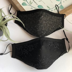 May include: Two black face masks. One mask is made of a black fabric with a small floral pattern. The other mask is made of black lace.
