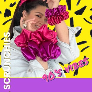 May include: A woman wearing a denim jacket and a pink and purple scrunchie on her wrist. She is also wearing a large pink scrunchie in her hair. The background is yellow with black scribbles and the text "90's VIBES" and "XXL SCRUNCHIES".