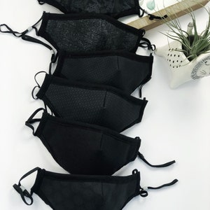 May include: A set of six black face masks with different patterns and textures. The masks are made of a breathable fabric and have adjustable ear loops.
