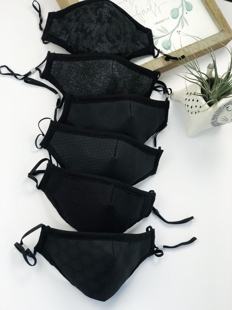 May include: A set of six black face masks with different patterns and textures. The masks are made of a breathable fabric and have adjustable ear loops.