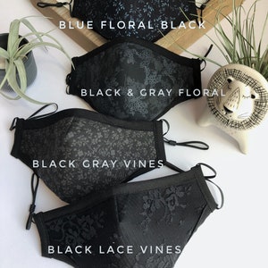 May include: Four black face masks with different patterns. The top mask has a blue floral pattern, the second mask has a black and gray floral pattern, the third mask has a black and gray vine pattern, and the bottom mask has a black lace vine pattern. The masks are arranged in a stack, with the top mask at the top of the image and the bottom mask at the bottom of the image. The text "LOVEAFFCO" is printed on the bottom mask.