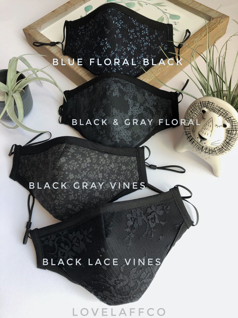 May include: Four black face masks with different patterns. The top mask has a blue floral pattern, the second mask has a black and gray floral pattern, the third mask has a black and gray vine pattern, and the bottom mask has a black lace vine pattern. The masks are arranged in a stack, with the top mask at the top of the image and the bottom mask at the bottom of the image. The text "LOVEAFFCO" is printed on the bottom mask.