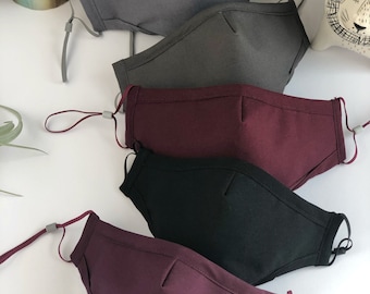 Op de afbeelding: Vijf gezichtsmaskers in verschillende kleuren, waaronder grijs, bordeauxrood en zwart. De maskers zijn gemaakt van een zachte, ademende stof en hebben verstelbare oorlussen.