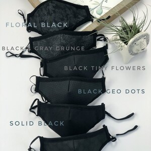 May include: Six black face masks with different patterns. The masks are arranged in a stack, with the top mask being a floral pattern, followed by a gray grunge pattern, a tiny flower pattern, a geometric dot pattern, a solid black mask, and a black mask with small circles. The text "Love never fails" is visible in the background.
