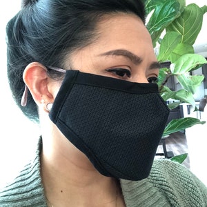 May include: A black face mask with a textured pattern. The mask is worn by a person with dark hair.