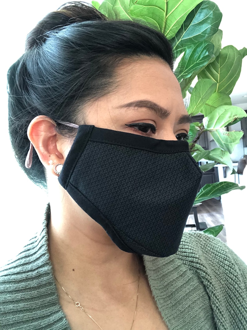 May include: A black face mask with a textured pattern. The mask is worn by a person with dark hair.