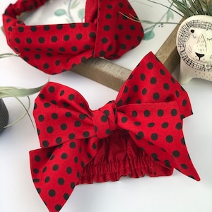 May include: Two red headbands with black polka dots. One headband has a bow, and the other has a twisted knot design. The headbands are made of fabric and are likely for fashion or hair accessories.