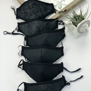 May include: Six black face masks with different patterns. The masks are made of a soft, breathable fabric and have adjustable ear loops.  The masks are stacked on top of each other.