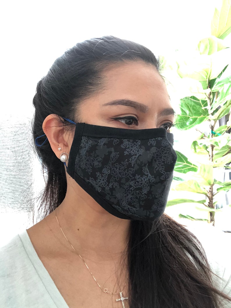 May include: A black face mask with a floral pattern. The mask is made of a soft, breathable fabric and has adjustable ear loops.