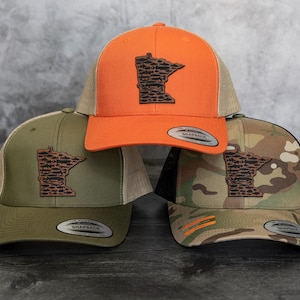 May include: Three trucker hats with a Minnesota state outline design. The hats are in orange, green, and camouflage.