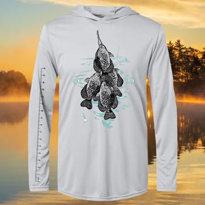 May include: A light gray long-sleeve performance fishing shirt with a black and white illustration of a group of crappie fish hanging from a fishing line. The shirt has a hood.