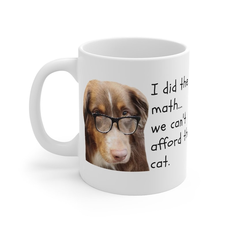 Puede incluir: Taza de caf&eacute; de cer&aacute;mica blanca con un perro marr&oacute;n y blanco que lleva gafas. El texto en la taza dice "Hice las cuentas... no podemos permitirnos el gato."