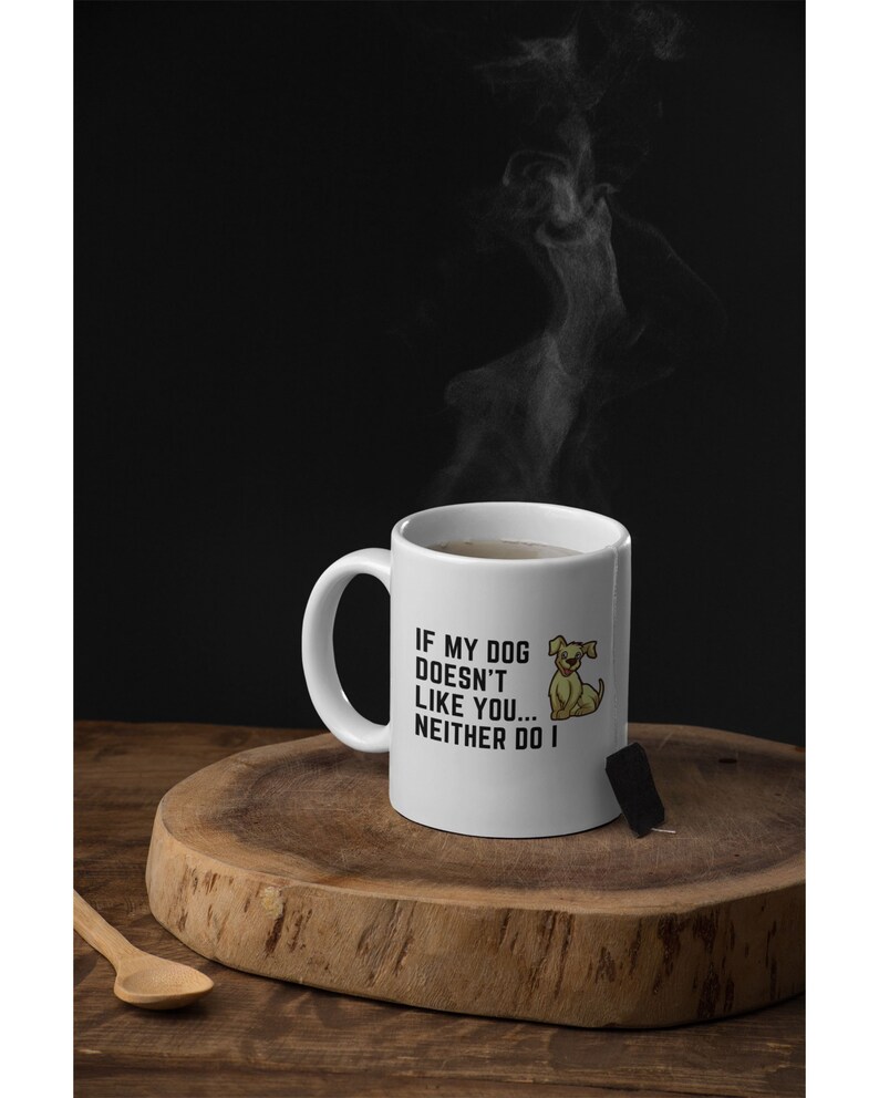 May include: White ceramic mug with a black and white graphic that says "If my dog doesn't like you... neither do I". A cartoon dog is pictured next to the text. The mug is sitting on a wooden surface with a tea bag next to it.