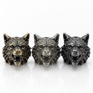 May include: Three metal beads shaped like snarling wolf heads arranged in a row. The left bead has a bronze finish, while the center and right beads feature a silver finish with dark, recessed detailing to highlight the fur and facial features.