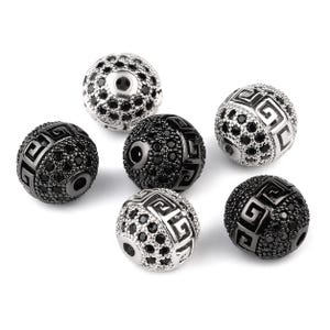 May include: Six decorative round beads. Some are black with geometric patterns and black accents. Others are silver with black accents and geometric patterns. The beads are on a white background.