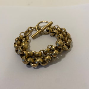 May include: A gold-toned chain bracelet with a toggle clasp. The bracelet is made of multiple strands of linked circles.