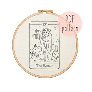 May include: A black and white embroidery pattern of the Hermit card from the tarot deck. The card features a hooded figure holding a lantern and a staff, standing in a mountainous landscape. The text "IX The Hermit" is printed at the top of the card.