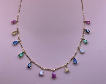 May include: A gold chain necklace with teardrop-shaped gemstones in various colors, including red, blue, green, yellow, and white.
