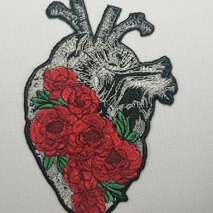Op de afbeelding: Een geborduurde strijkpatch met een gedetailleerd anatomisch hart met rode rozen en groene bladeren.