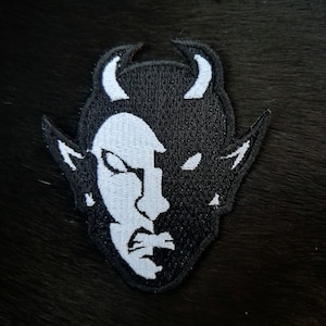 Op de afbeelding: Zwart-witte geborduurde patch van een duivels gezicht met hoorns.