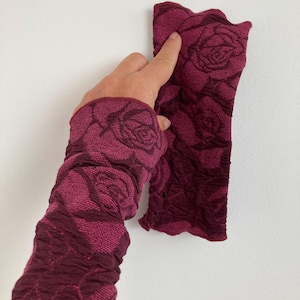 Könnte beinhalten: Bordeauxfarbene Armstulpen mit Rosenmuster. Der Stoff hat ein strukturiertes, plissiertes Aussehen. Die Armstulpen sind tiefrot-violett.