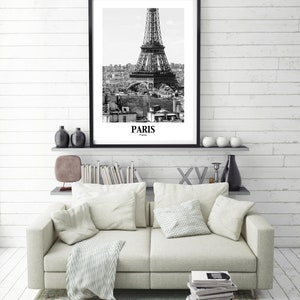 May include: Black and white framed print of the Eiffel Tower in Paris, France. The print is displayed above a light-colored sofa with pillows and a patterned throw. The word "Paris" is printed at the bottom of the print.