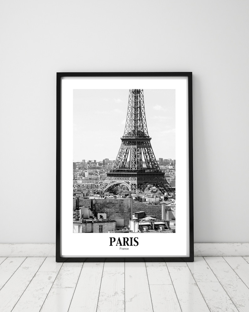 May include: Black and white framed print featuring the Eiffel Tower in Paris. The iconic landmark is centered, with the city skyline in the background. The word "PARIS" is printed at the bottom.
