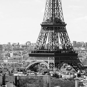 May include: Black and white photograph of the Eiffel Tower in Paris, France. The iconic wrought-iron lattice tower dominates the frame, with the city skyline and buildings in the background. The image is a high-angle shot.