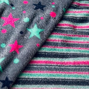 May include: Close-up of two plush fabrics. One is gray with pink, teal, and navy stars and dots. The other is striped with pink, teal, and navy blue. The fabrics appear soft and cozy, suitable for blankets or loungewear.