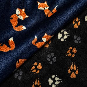 Könnte beinhalten: Zwei Stoffe mit Tiermustern. Einer ist marineblau mit orangefarbenen Füchsen, der andere ist schwarz mit Pfotenabdrücken. Die Füchse haben weiße Akzente. Die Pfotenabdrücke sind orange und weiß.