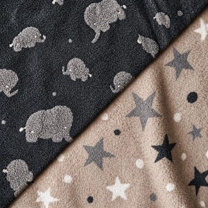 May include: A close-up of two sections of a soft blanket. One section is dark gray with light gray elephant patterns. The other section is tan with gray stars and white polka dots. The blanket has a plush texture.