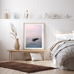 K&ouml;nnte beinhalten: Ein gerahmter Druck eines Wals, der bei Sonnenuntergang aus dem Wasser springt. Der Druck h&auml;ngt an einer wei&szlig;en Wand &uuml;ber einer Holzbank und einem braunen Teppich.