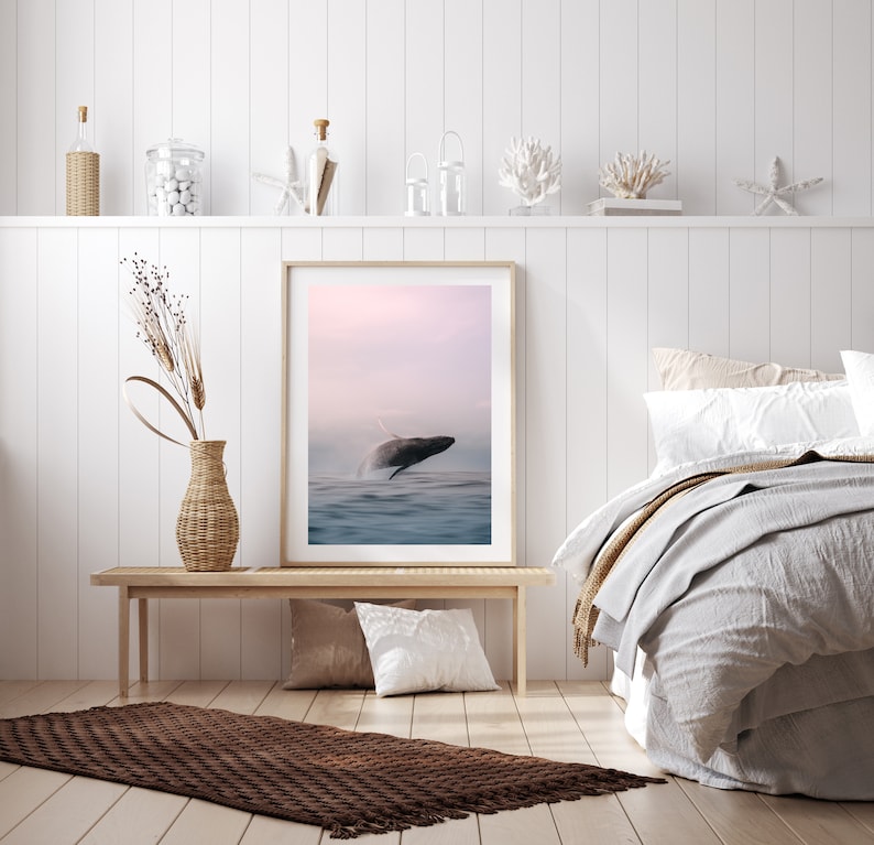 K&ouml;nnte beinhalten: Ein gerahmter Druck eines Wals, der bei Sonnenuntergang aus dem Wasser springt. Der Druck h&auml;ngt an einer wei&szlig;en Wand &uuml;ber einer Holzbank und einem braunen Teppich.