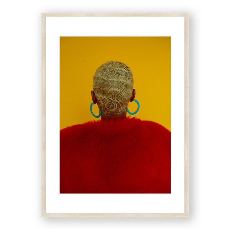 May include: A person with short, blonde, wavy hair wearing large, turquoise hoop earrings and a red fur coat against a yellow background.