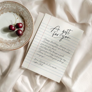 May include: A greeting card with the text "A gift for you" in elegant script. The card is on lined paper and includes a handwritten birthday message. Three cherries rest on a decorative plate.