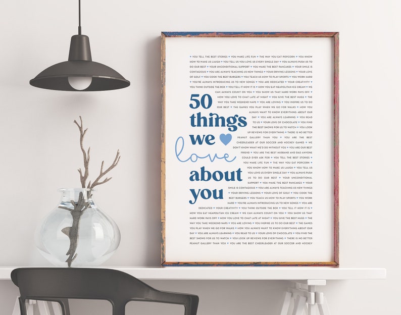 May include: A framed print with a blue and white design that says "50 things we love about you". The print is on a white background and is surrounded by a wooden frame.