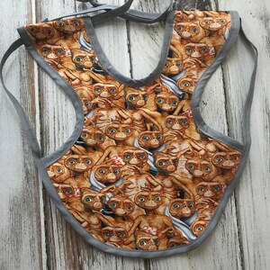 May include: A gray bib with a pattern of brown aliens from the movie E.T. The Extra-Terrestrial. The bib has a tie closure.