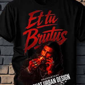 May include: Black t-shirt with the red text "Et tu, Brutus" above an illustration of a person lighting a cigarette. The shirt also features the text "PHAT URBAN DESIGN" and "EST. 2023 | HANDMADE DESIGNS".