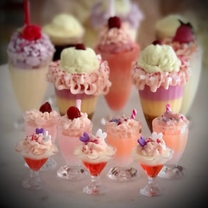 Puede incluir: Una colección de mini sundaes de helado con capas rosas, blancas y amarillas, cubiertas con chispas y una variedad de caramelos coloridos. Los sundaes se muestran en platos de vidrio transparente con una variedad de ingredientes.