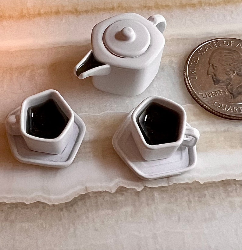 May include: A set of white ceramic teacups and teapot with a hexagonal shape. The cups are filled with black liquid and have a saucer. The teapot has a lid and a spout.
