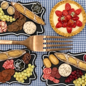 Puede incluir: Dos bandejas de servir de pizarra negra con varios alimentos, que incluyen pan, queso, uvas y tartas de frutas. Un tenedor de plata se coloca encima de las bandejas.