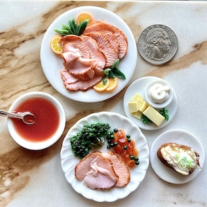 Op de afbeelding: Een miniatuur Thanksgiving-dinerset met een wit bord met gesneden kalkoen, een wit bord met een bijgerecht van boter en kruiden, een wit bord met een bijgerecht van aardappelpuree, een wit bord met een bijgerecht van cranberry-saus en een witte kom met jus.