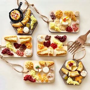 May include: Five miniature wooden cheese boards with various cheeses, crackers, grapes, and other snacks. The boards are decorated with red and white accents and are perfect for a party or gathering.