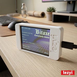 Op de afbeelding: Een witte Bitaxe cryptocurrency mining-apparaat met een scherm dat gegevens weergeeft, waaronder "BTC: 72118 USD" en "Every hash counts". Het apparaat is aangesloten op een zwarte kabel en heeft het "lezyi" logo.