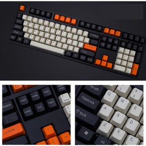 Pode incluir: Um teclado mecânico preto com uma mistura de teclas brancas, laranja e pretas. O teclado tem um layout padrão com um teclado numérico e teclas de função. As teclas são uma mistura de cores, com teclas laranja.